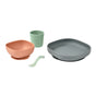 A set of childrens dishware including a peach bowl, a green cup, a gray plate, and a small green spoon, all made of smooth, matte plastic, displayed on a white background.