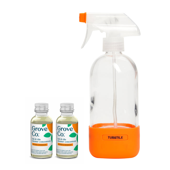 The Tub & Tile Cleaner Starter Set by Grove Co. includes a clear spray bottle with an orange base labeled TUB&TILE and two bottles of plant-based cleaner concentrate, crafted for use in your reusable glass spray bottle with a green leaf design.