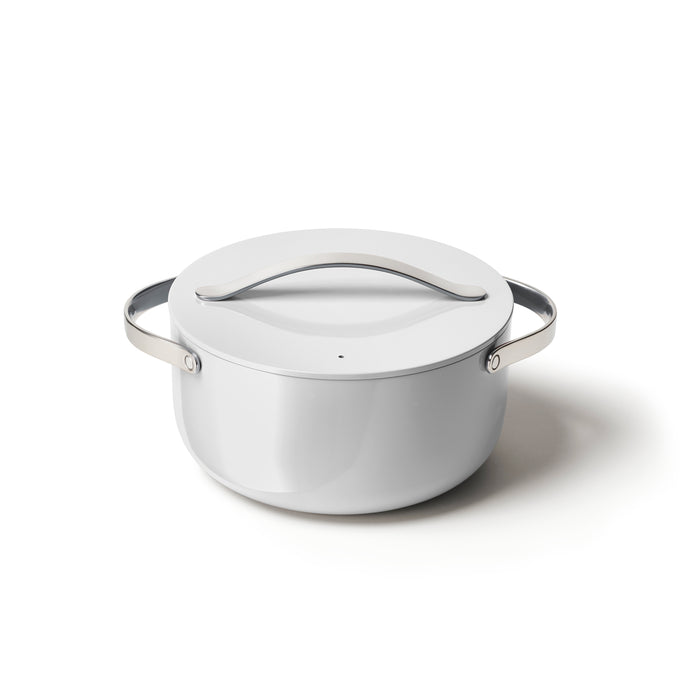 A white, round pot with a matching lid and metal handles on each side, placed on a white surface.
