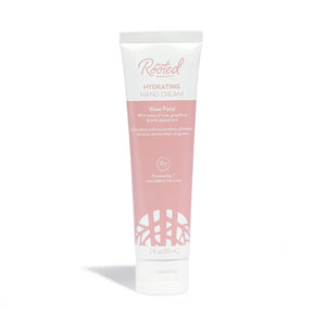Rooted Beauty Hydrating Hand Cream in Rose Petal scent, packed with plant-based moisturizers and shea butter, comes in white and pink packaging highlighting pink grapefruit and pink peppercorn. Perfect for dry skin, this 2 fl oz (59 mL) cream offers lush hydration.