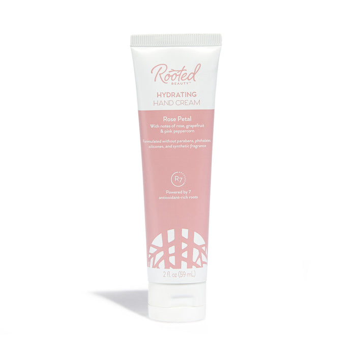 A tube of Rooted Beauty Hydrating Hand Cream in Rose Petal scent, featuring a white cap and a pink-and-white label with product details and branding. The tube contains 2 fl oz (59 mL).