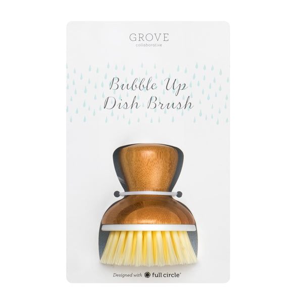 A wooden dish brush with light bristles is displayed in plastic packaging labeled Grove Collaborative Bubble Up Dish Brush, with blue raindrop graphics in the background.