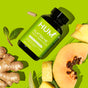 A Flatter Me Fast - For Bloat Relief bottle by HUM Nutrition, designed to reduce bloating with digestive enzymes, is surrounded by ginger, mint leaves, a pineapple wedge, halved papaya on a bright yellow background. A single capsule is beside the bottle.
