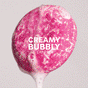 A vibrant pink loofah with frothy bubbles is centered against a light gray background. Bold white text reading CREAMY BUBBLY LATHER evokes the smooth sensation of NOT!CE Hair Cos ALINE Shampoo Bar, offering plastic-free hair care for frizz control.