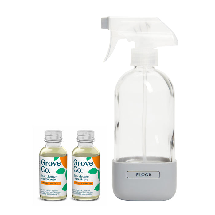 The Grove Co. Floor Cleaner Starter Set includes a clear, reusable bottle labeled Floor with a white trigger and two small bottles of plant-based Grove Co. floor cleaner concentrate. The transparent bottles are filled with yellow liquid and have green and white labels.