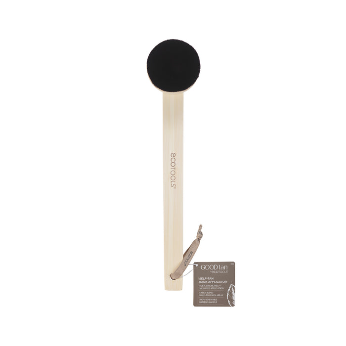 A soft, round black applicator brush with a long, light wooden handle labeled ECOTOOLS. A small brown Goodtan product tag is attached to the handle with a string. The background is white.