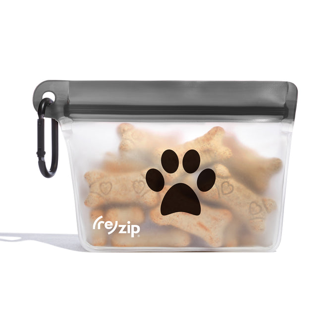 The (re)zip Airtight Pet Treat Bag + Carabiner is a reusable, clear zippered bag with a gray top and black paw print, filled with bone-shaped treats. Water-resistant and perfect as a leash accessory.