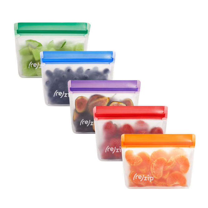 Five (re)zip Reusable Leakproof Snack Stand Up Bags, each with a different colored zipper (green, blue, purple, red, orange), are filled with sliced fruits and arranged diagonally. Airtight design keeps snacks fresh and secure.