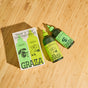 Two green-labeled bottles of Graza’s The Duo Drizzle and Sizzle Olive Oil Gift Set sit beside a coordinating box on a light wood surface. Featuring vibrant illustrations and bold lettering, this gift set makes a striking addition to any gourmet condiment collection.