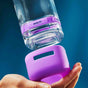 A hand fits a Grove Collaborative Tub & Tile Cleaner Starter Sets reusable glass spray bottle with a purple sleeve on, set against a blue background.