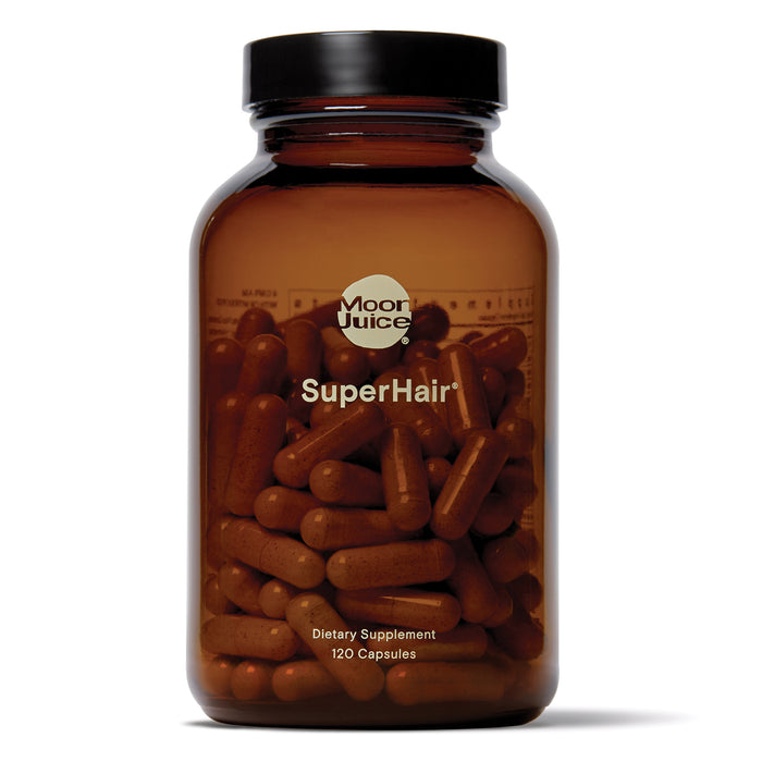 A brown glass bottle labeled Moon Juice SuperHair containing 120 dietary supplement capsules, with the capsules visible through the transparent bottle.