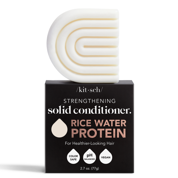 A solid conditioner bar with a curved, geometric design sits on top of a black box labeled Strengthening Solid Conditioner, Rice Water Protein by Kitsch; the box notes it is color-safe, pH balanced, and vegan.
