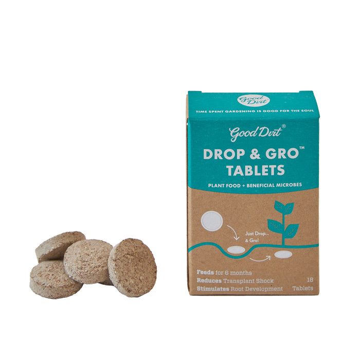A box labeled Good Dirt Drop & Gro Tablets plant food stands upright next to four round, brown tablets. The packaging highlights benefits like feeding for 6 months and reducing transplant shock.