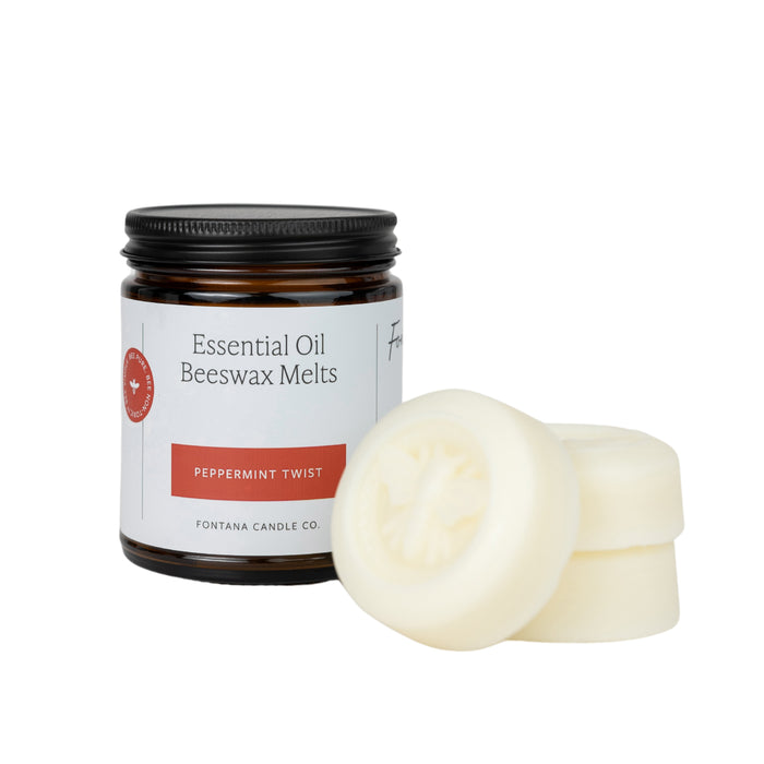 A jar labeled “Essential Oil Beeswax Melts, Peppermint Twist” from Fontana Candle Co. sits beside three white, round beeswax melts stacked slightly in front of the jar.