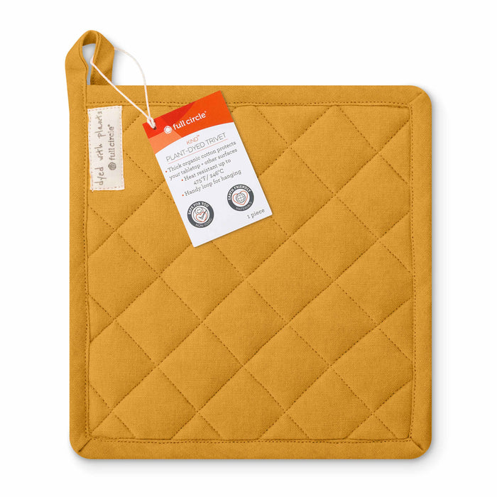 A mustard yellow, quilted pot holder with a hanging loop in the top left corner and product tags attached. The tags describe it as a plant-dyed trivet made by Full Circle.