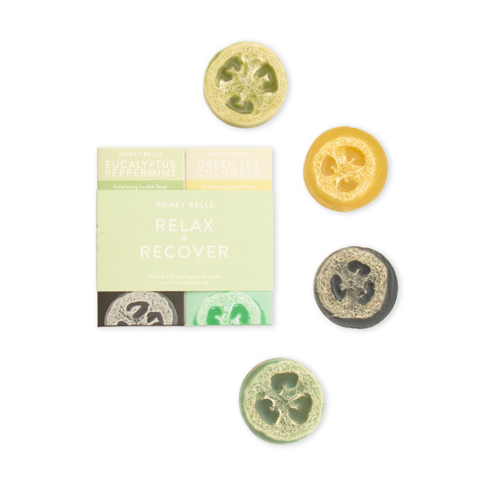 Four round loofah soaps, each a different color, are arranged beside a pastel box labeled “Honey Belle Relax + Recover” featuring eucalyptus peppermint and green tea cucumber varieties.