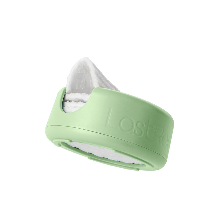 A reusable makeup remover pad in a light green storage case, partially visible against a white background. The pad appears soft and white, designed for sustainable beauty routines.