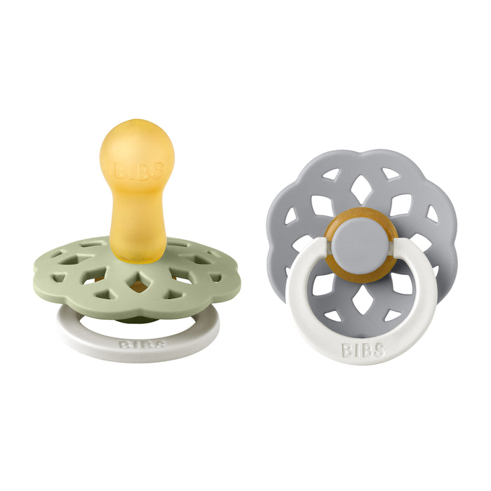 Two baby pacifiers are shown. One has a yellow nipple, green guard, and white handle, while the other has a gray, flower-shaped guard with a yellow accent and a white ring handle. Both have BIBS branding.