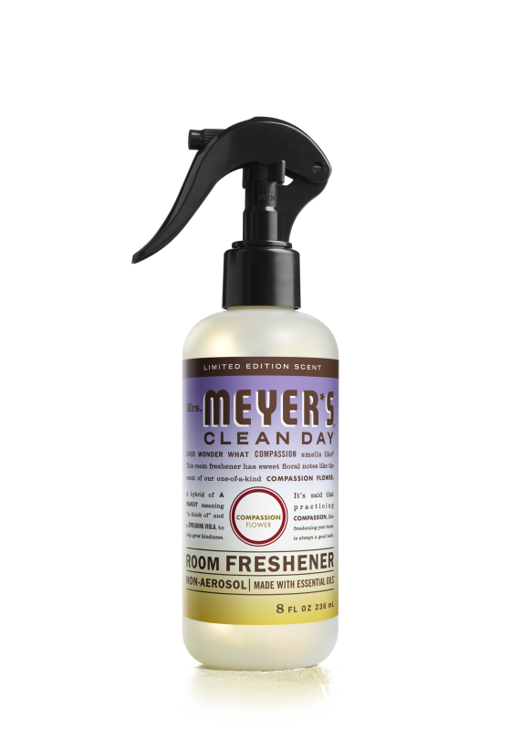 Mrs. Meyers Room Freshener features a black spray nozzle, an 8 fl oz bottle with a purple and yellow label showcasing the limited edition Compassion Flower scent made with essential oils, offering a refreshing, non-aerosol experience.