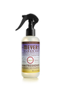 Mrs. Meyers Room Freshener features a black spray nozzle, an 8 fl oz bottle with a purple and yellow label showcasing the limited edition Compassion Flower scent made with essential oils, offering a refreshing, non-aerosol experience.