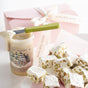 A Pumpkin & Winter White Whipped Duo from Savannah Bee Company, paired with a green-handled knife and pistachio nougat on a white tray, is framed by a pink ribboned gift box for a festive seasonal scene.