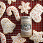 A jar of Savannah Bee Company Winter White Whipped Honey with a creamy texture sits on a wire rack, surrounded by iced holiday cookies in festive shapes—stars, candy canes, and hearts—decorated with red, gold, and white sprinkles.