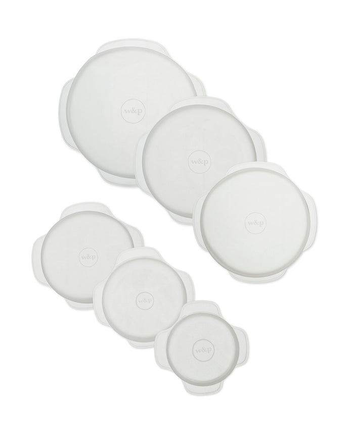 Six round, white silicone stretch lids of various sizes are arranged in two columns on a white background. Each lid has handles on the sides and the w&p logo in the center.