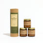 A Seasonal Mini Candle Gift Set featuring a cylindrical cardboard tube next to three mini candles in amber glass with gold lids.