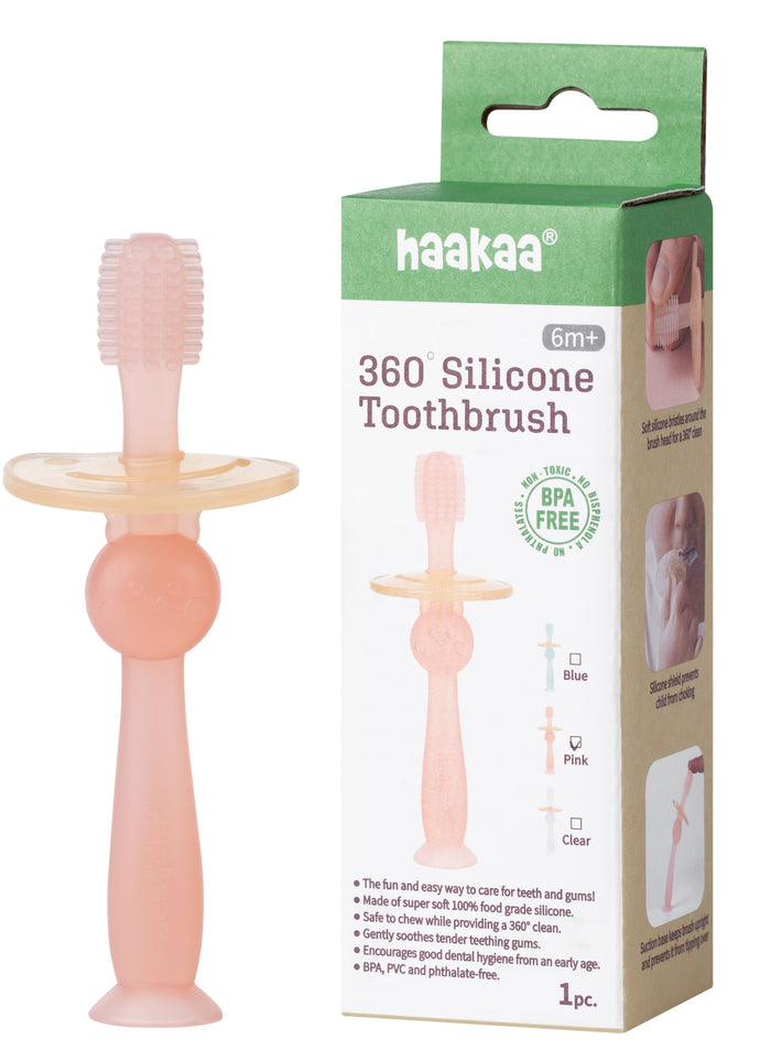 A pink silicone baby toothbrush with a wide safety guard stands upright next to its box, which displays the product name haakaa 360° Silicone Toothbrush and information for ages 6 months and up.