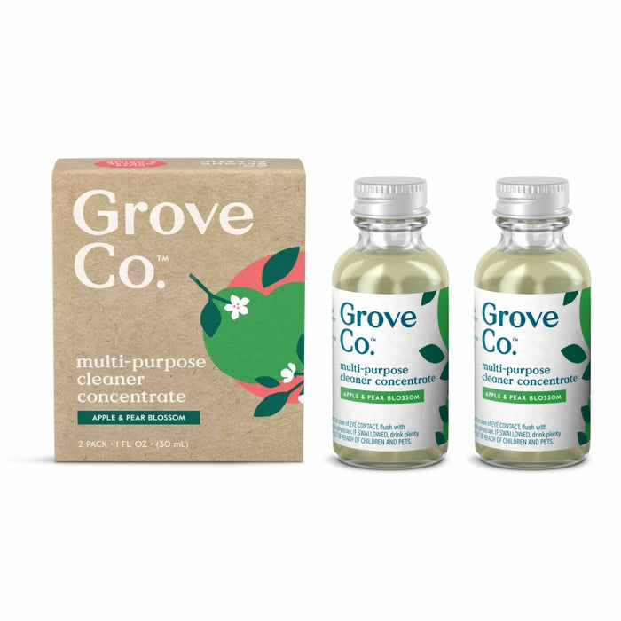 Two small glass bottles of Grove Co. multi-purpose cleaner concentrate, labeled Apple & Pear Blossom, stand beside a brown box with matching branding and fruit illustrations.