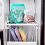 Reusable silicone food bags filled with greens, nuts, and various frozen foods are neatly organized on the shelves inside a freezer. The bags are in different colors and sizes.