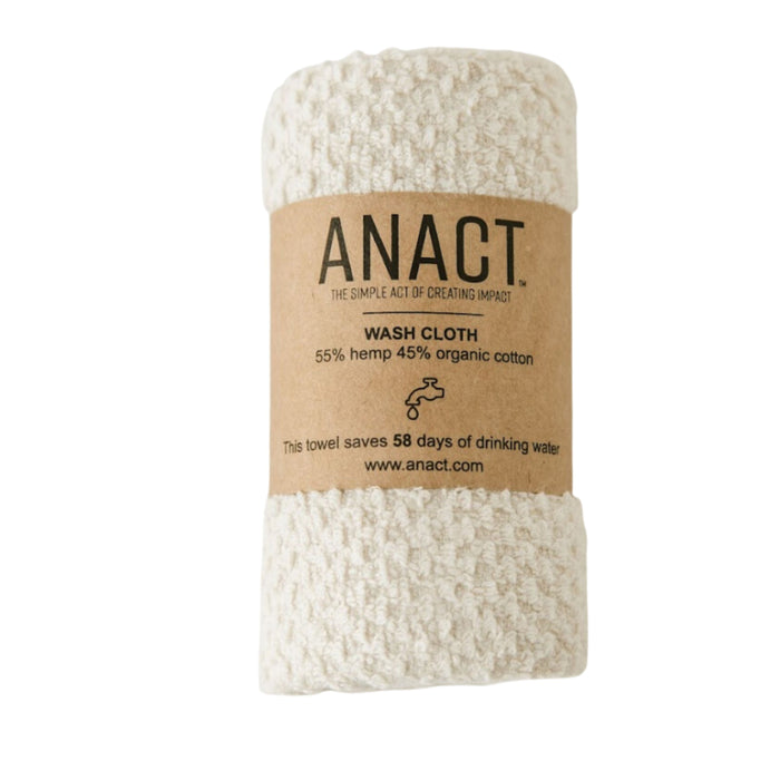 A rolled, off-white textured wash cloth wrapped in a brown paper label that reads ANACT. WASH CLOTH, 55% hemp 45% organic cotton, with information about its water-saving benefits.