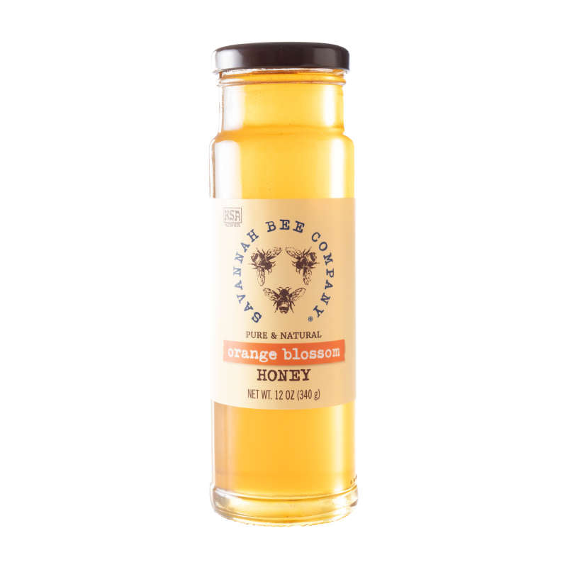 The Savannah Bee Companys Orange Blossom Honey, in a tall, clear glass jar, displays a light amber color. It has a subtle citrus aroma and is labeled as Pure & Natural with a net weight of 12 oz (340 g).