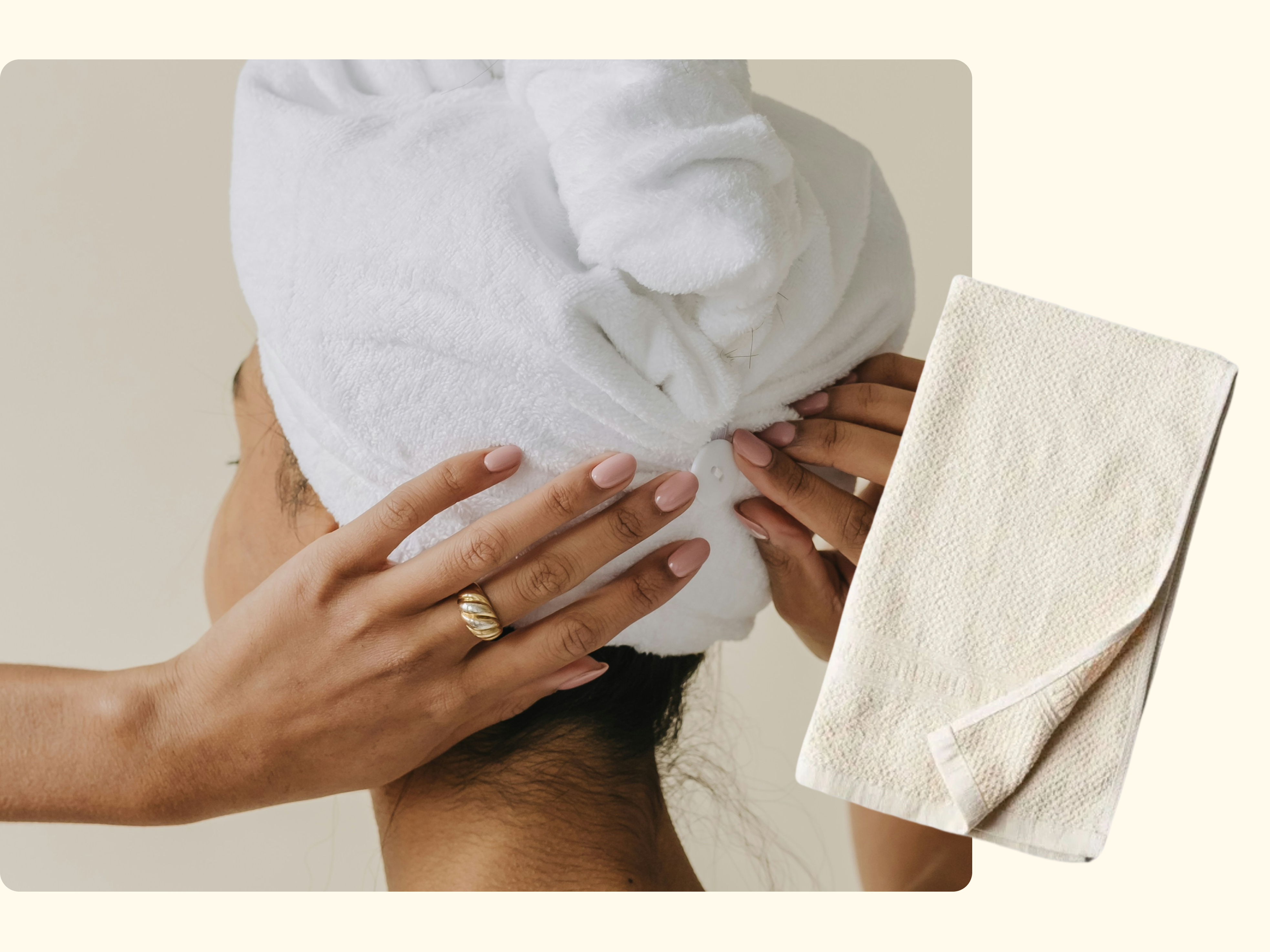 A person with a towel wrapped around their head adjusts it with their hands. Their nails are manicured and they wear a gold ring. An off-white textured towel is displayed beside them on a light background.