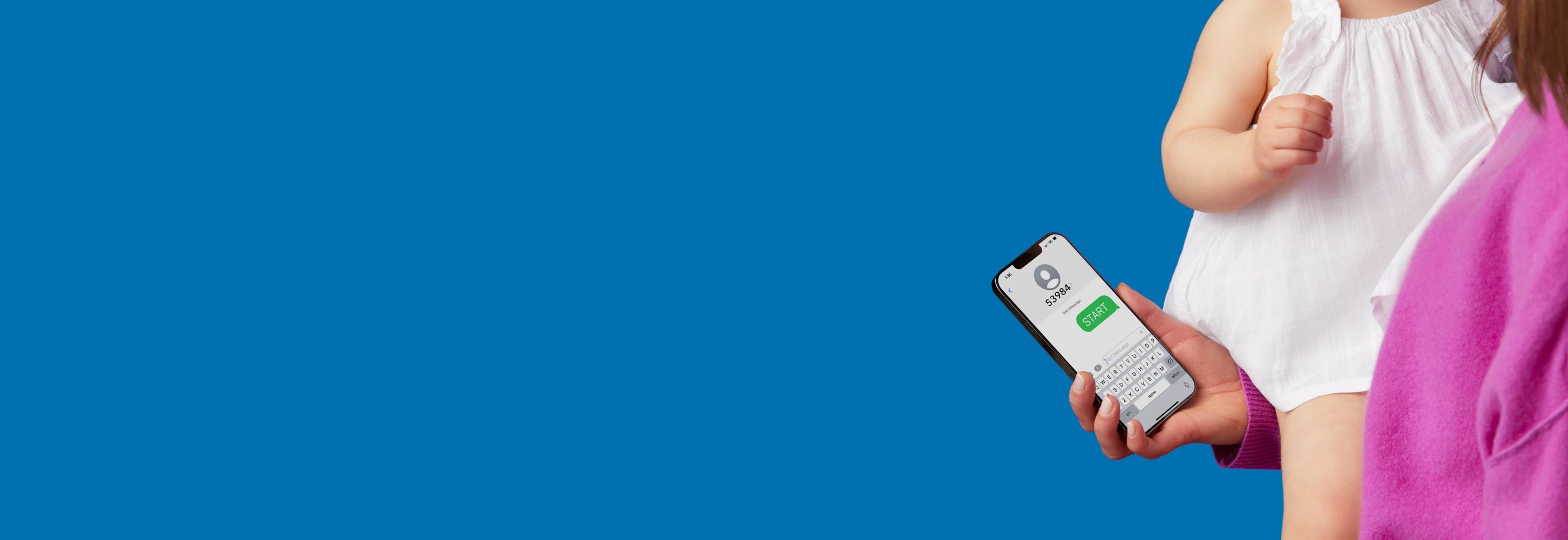 A person holding a baby is using a smartphone to send a message while standing against a solid blue background. The baby is wearing white, and only the upper body of both are visible.