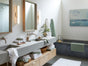 Modern bathroom with double sink, Coyuchi Air Weight® Organic Towels, a potted plant, wall mirrors, tub with green towel, and abstract art on the wall. Light wood cabinets and white walls create a clean, serene atmosphere.