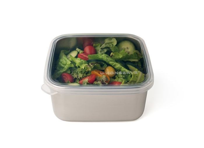 A stainless steel container with a clear plastic lid, filled with a fresh salad including lettuce, cherry tomatoes, cucumber, and green bell pepper slices.