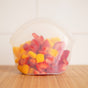 The Hugger Bag by Food Huggers, dishwasher safe and easy to clean, holds freshly cut strawberries and mango pieces on a wooden surface against a plain white background.