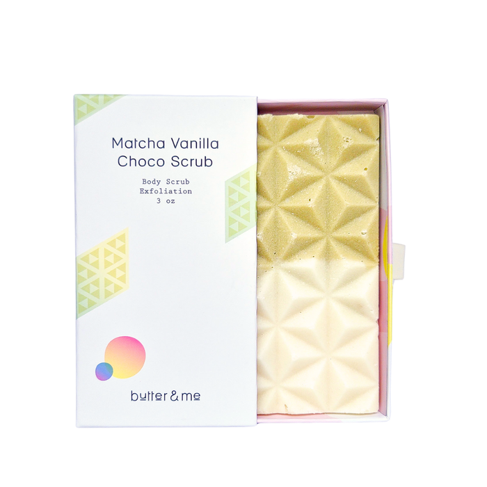 A box of Matcha Vanilla Choco Scrub by butter & me, partially open to reveal a geometric-patterned scrub bar in shades of green and cream. The box features minimalist design and soft pastel accents.