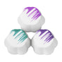 Three white, flower-shaped bath bombs with colorful brushstroke patterns on top: one purple, one teal, and one with two shades of purple. The bath bombs are arranged in a triangular formation.