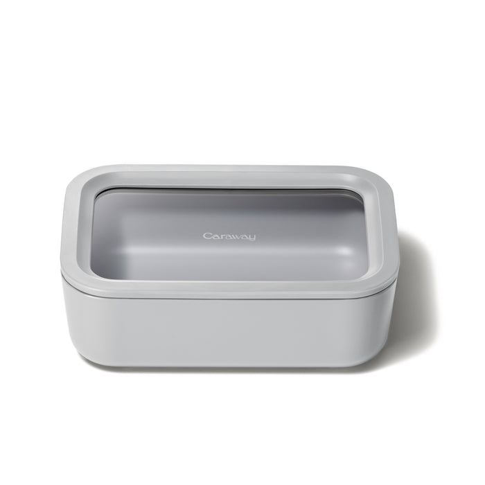 A rectangular, light gray food storage container with a clear lid and the word Caraway printed on top, placed on a white background.