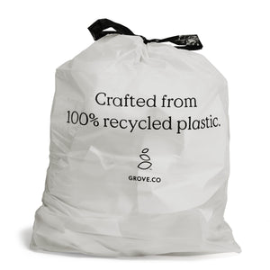 A crumpled white 13-gallon trash bag by Grove Co., features black drawstring handles and text stating Crafted from 100% recycled plastic. Below the text is a logo with two leaf-like shapes and GROVE.CO wording.