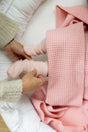 Hands adjust pink socks on a baby’s feet tucked under a textured, plant-dyed merino wool The Popcorn Blanket - Pink Quartz.