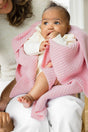 An adult holds a baby wrapped in a soft, pink, textured The Popcorn Blanket - Pink Quartz superfine merino baby blanket.