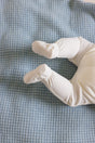 A baby wearing cream-colored footed pants lying on a sky blue The Popcorn Blanket - Sky Blue superfine merino baby blanket.