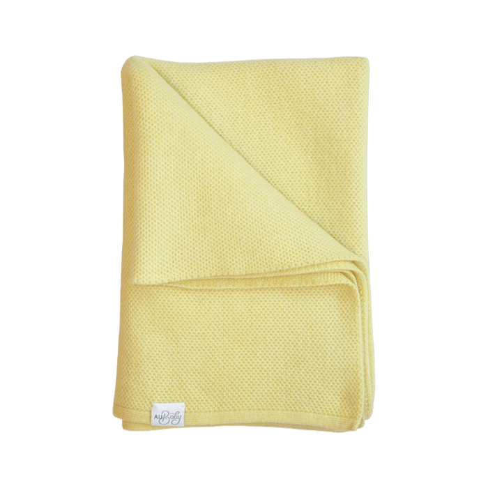 Folded pale yellow The Sawa - Citron merino baby blanket with a subtle textured pattern and personalized embroidery.