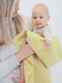 A woman holds a baby wrapped in a personalized embroidered The Sawa - Citron merino baby blanket.