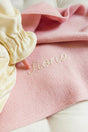 A child’s finger points to the name Fiona embroidered in cursive thread on a textured The Sawa - Pink Quartz baby blanket.