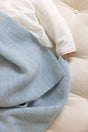 An infant’s hand rests on a light blue The Sawa - Sky Blue merino baby blanket.