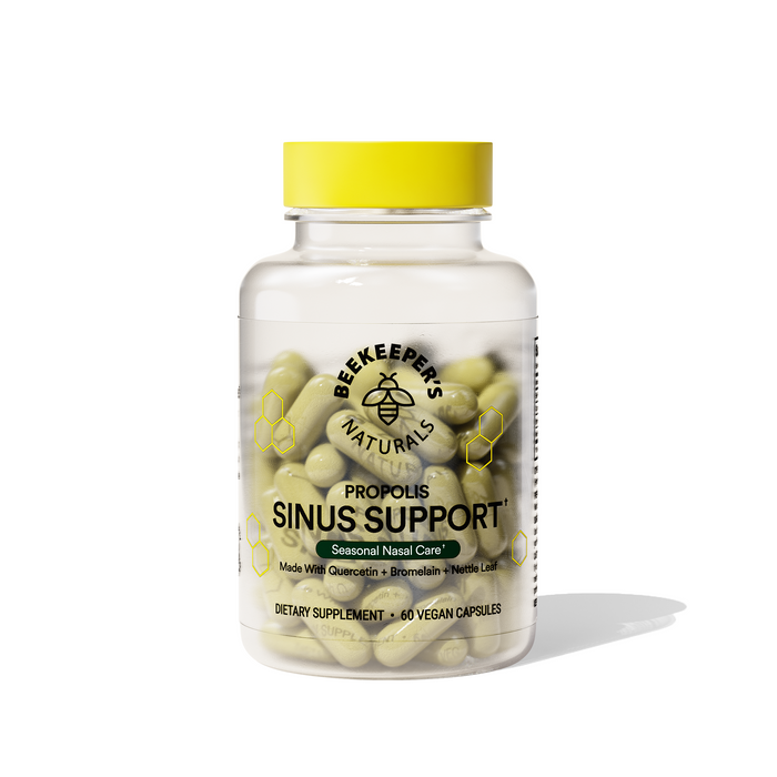 A clear bottle labeled Beekeepers Naturals Propolis Sinus Support contains green capsules. The label mentions Seasonal Nasal Care, vegan capsules, and dietary supplement. The bottle has a yellow cap.